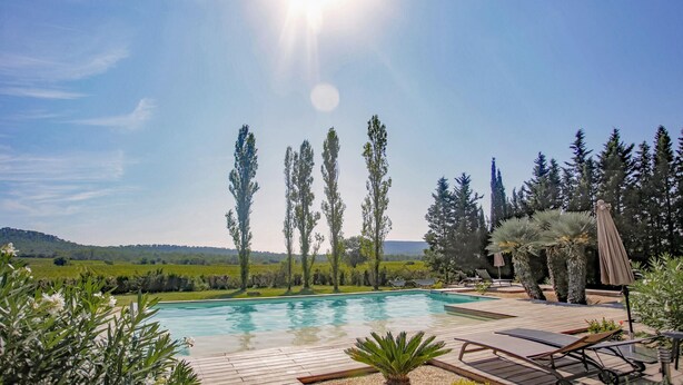 A swimming pool with a wooden deck, surrounded by tall trees and a clear sky. - Gorgeous home in Carnas (Carnas)