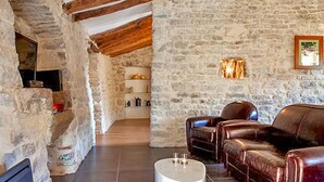 A rustic stone-walled room with exposed wooden beams, a fireplace, leather sofas, and a tiled floor. - Gorgeous home in Carnas (Carnas)