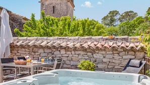 A stone wall with a tiled roof, a hot tub, outdoor furniture, and a tower in the background. - Gorgeous home in Carnas (Carnas)