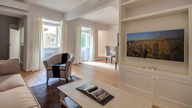 Een ruime woonkamer met een bank, een salontafel met een tijdschrift, een eethoek met stoelen en een groot schilderij aan de muur.