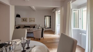 Een eetgedeelte met een tafel voor vier personen, een bank op de achtergrond en een raam met gordijnen.