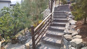 Eine steinerne Treppe mit hölzernem Geländer, umgeben von Steinen und Bäumen.