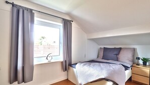 Een slaapkamer met een bed, nachtkastje, raam met gordijnen en uitzicht.