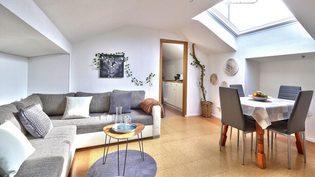 Een moderne woonkamer met een bank, salontafel en een eettafel met stoelen. Er is een dakraam boven de eethoek.