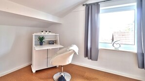 Een kamer met een witte stoel, een witte kast met planken, een kamerplant en een raam met gordijnen.