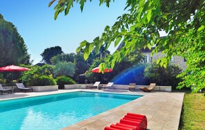 A swimming pool with lounge chairs and umbrellas, surrounded by greenery and a stone building in the background. - Gorgeous home in Velines with WiFi (Velines)