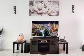 A flat-screen TV on a wooden entertainment center, with a floral painting above it and a decorative glass lamp on the left.