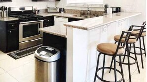 A modern kitchen with a central island, stainless steel appliances, and bar stools. - Panoramic Strip Views ~ Spacious, Gorgeous Home! (Las Vegas)