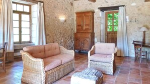 A rustic room with stone walls, two wicker sofas, a wooden cabinet, and a window with curtains. - Gorgeous home in CAMPSEGRET with WiFi (CAMPSEGRET)
