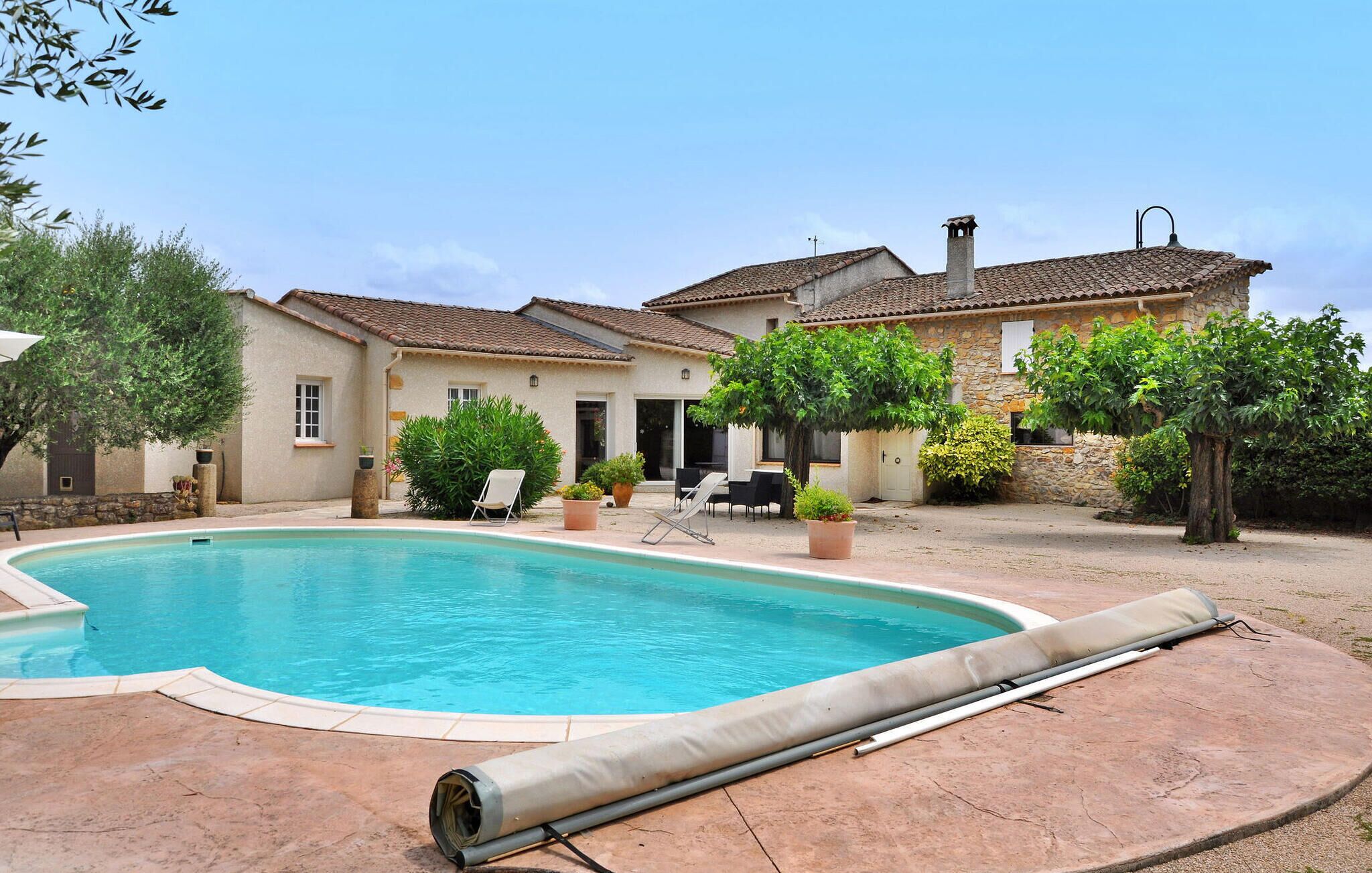 A pool area with a stone house, outdoor seating, and potted plants.