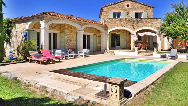 A two-story stone house with a swimming pool, outdoor seating, and a garden.