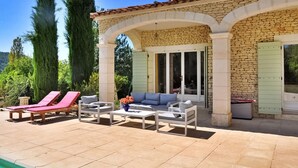 A covered outdoor seating area with stone walls, a pool, and lounge chairs.