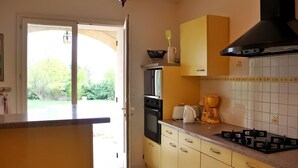 A kitchen with a gas stove, oven, and coffee maker. There is a door leading to a garden.