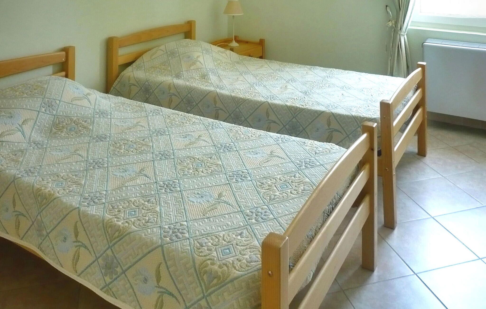 Twee enkele bedden met houten frames en beddengoed met een patroon in een kamer met betegelde vloer.