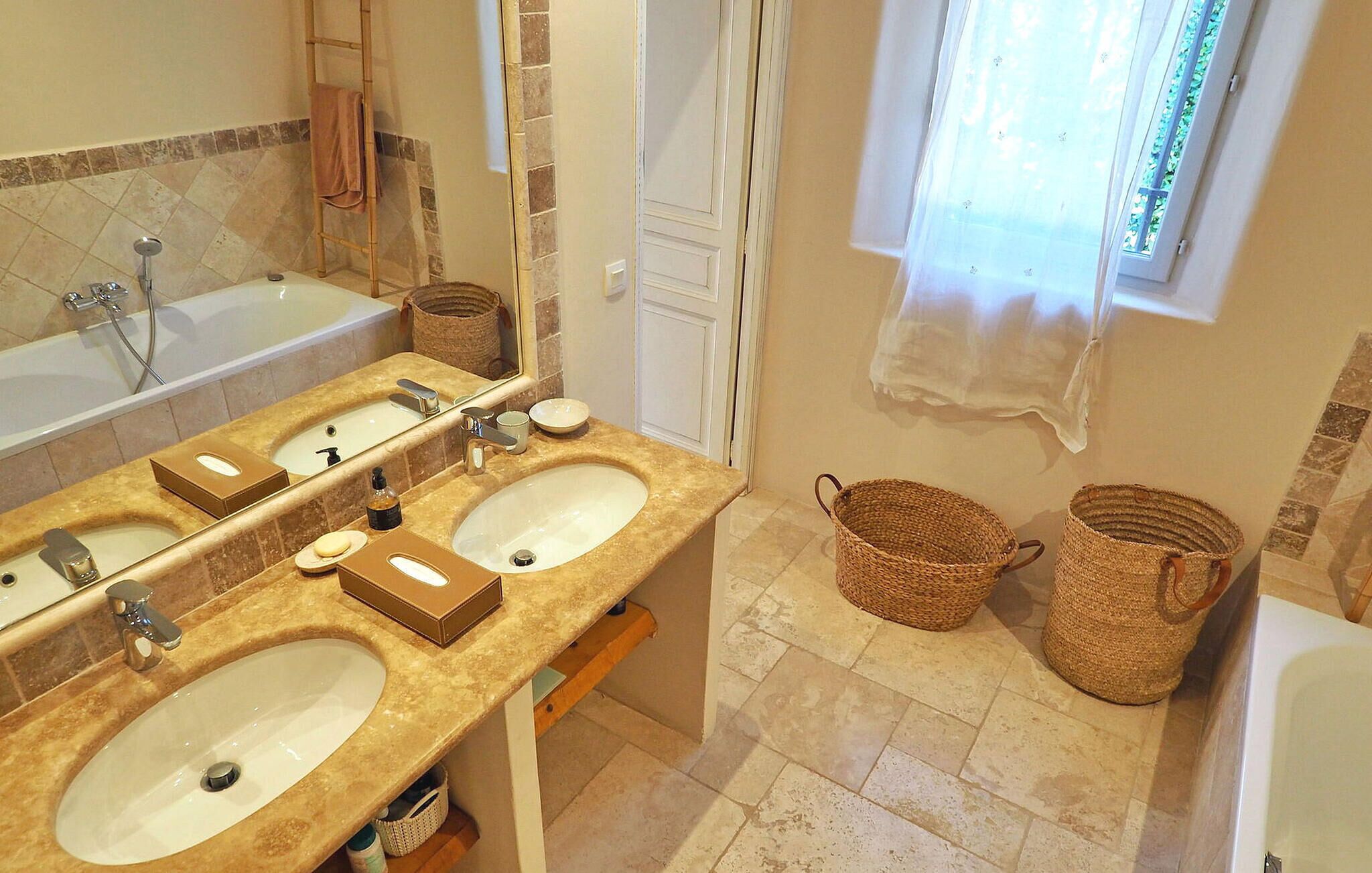 A bathroom with two sinks, a bathtub, and a window with a sheer curtain.