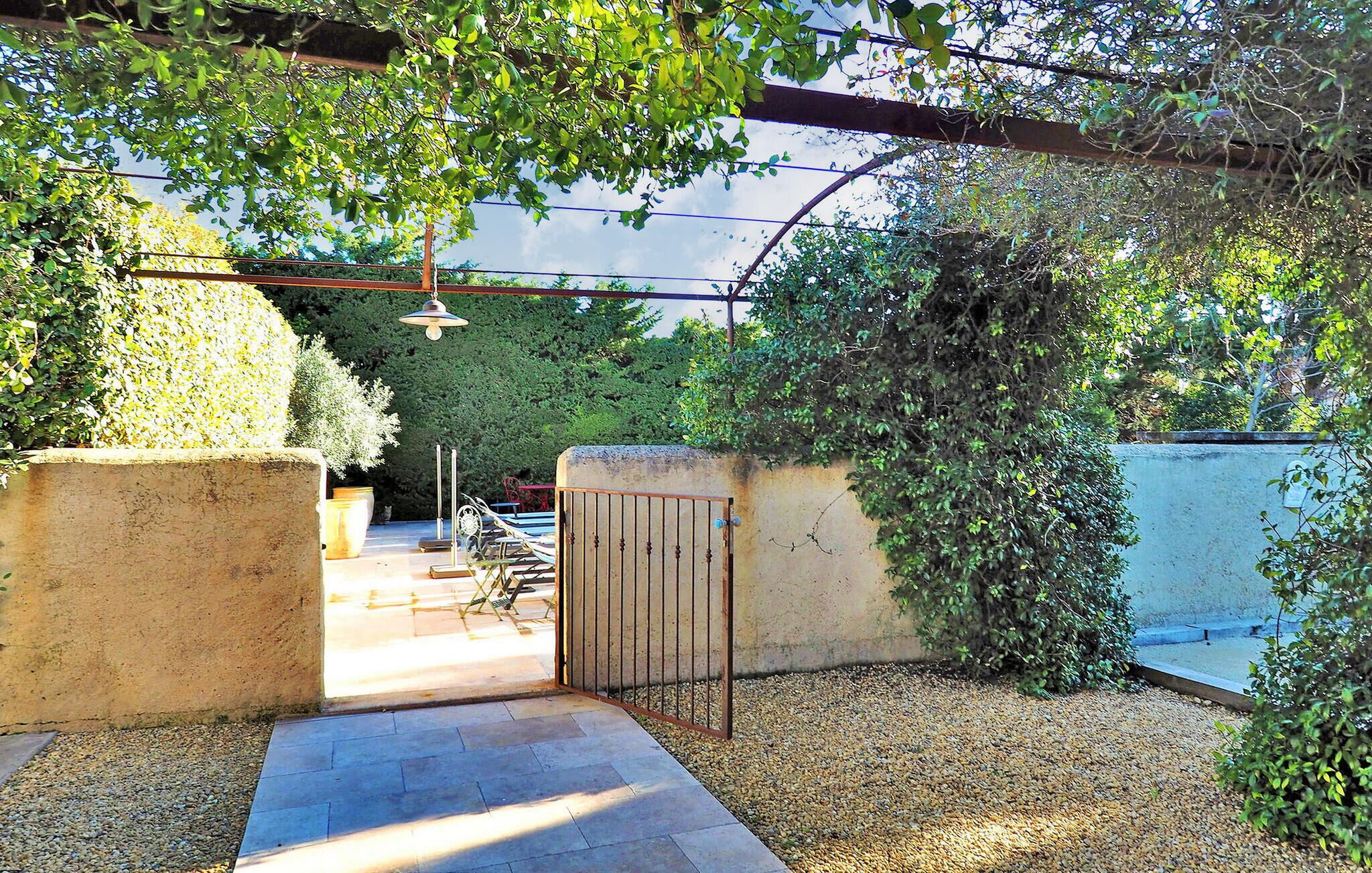 Un jardin clos par un portail, avec un espace patio, entouré d’une végétation luxuriante et agrémenté d’une pergola.