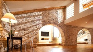 Un loft espacioso con paredes de piedra vista, vigas de madera y un gran ventanal abovedado que deja entrar luz natural.