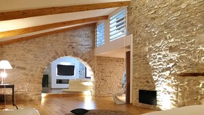 Un loft espacioso con paredes de piedra vista, vigas de madera y un techo alto.