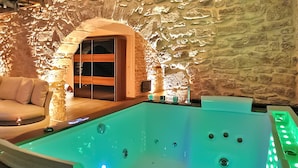 Zona de spa con un jacuzzi, un banco de madera y una pared de piedra.