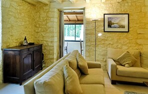 Una sala de estar con una pared de piedra, un mueble de madera, un sofá beige, una lámpara de pie y un cuadro en la pared.
