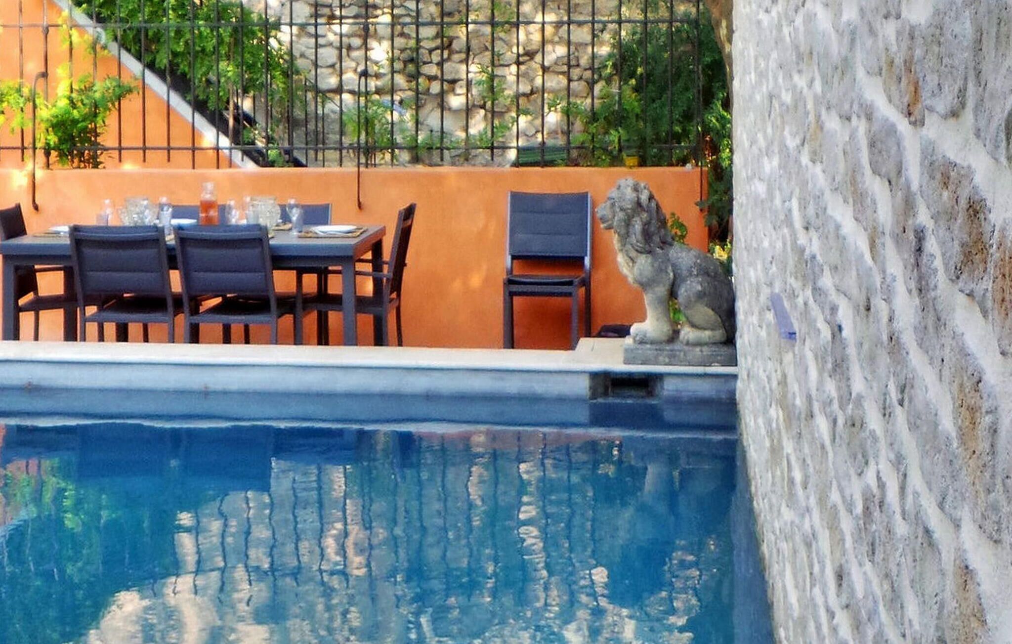 Un área de comedor junto a la piscina, con una mesa, sillas, una estatua de piedra y un muro de piedra.