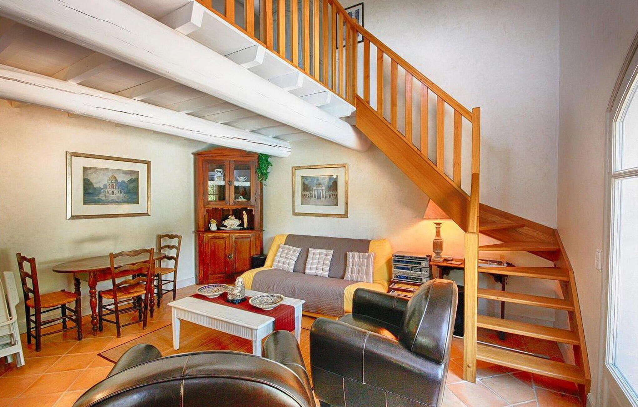Een gezellige woonkamer met een houten trap, een eethoek met stoelen en een tafel, en een boekenkast.