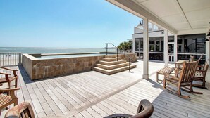 Une terrasse en bois agrémentée d’un jardinier en pierre, d’un espace salon extérieur et offrant une vue sur l’océan.