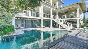 Una casa de dos pisos con piscina, mobiliario exterior y una escalera que lleva al nivel superior.