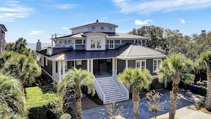 A two-story house with a covered porch, a staircase leading to the entrance, and palm trees in the yard.