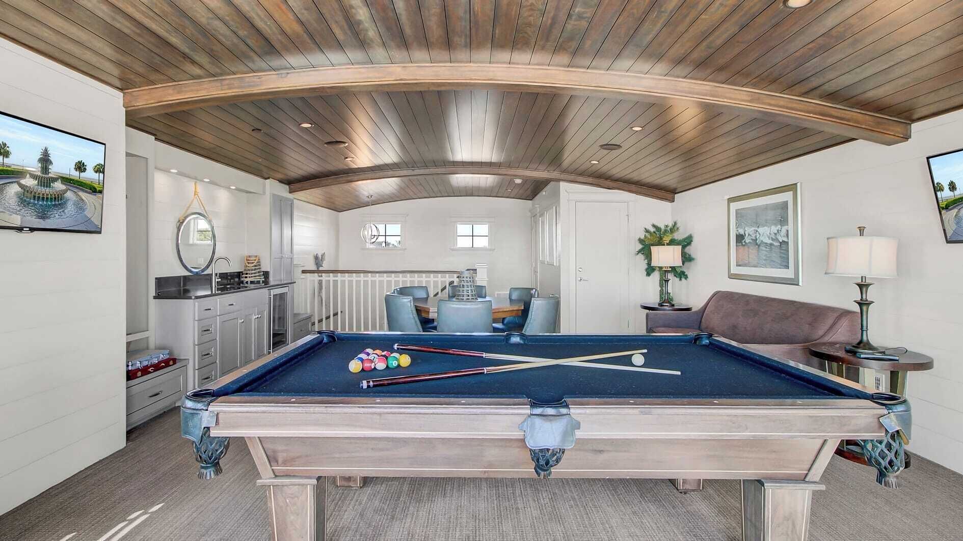 A pool table with balls, a sofa, a lamp, and a dining area with chairs.