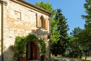 A stone building with arched windows and a clock, surrounded by trees.