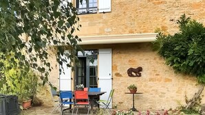 Un bâtiment en pierre doté d’un petit espace extérieur aménagé avec une table, des chaises et un pot de fleurs.
