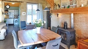 Une cuisine rustique avec une table en bois, des chaises, un poêle et un coin repas agrémenté d’un vase de fleurs.