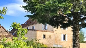 Un bâtiment en pierre avec un toit en tuiles, de nombreuses fenêtres et un arbre au premier plan.