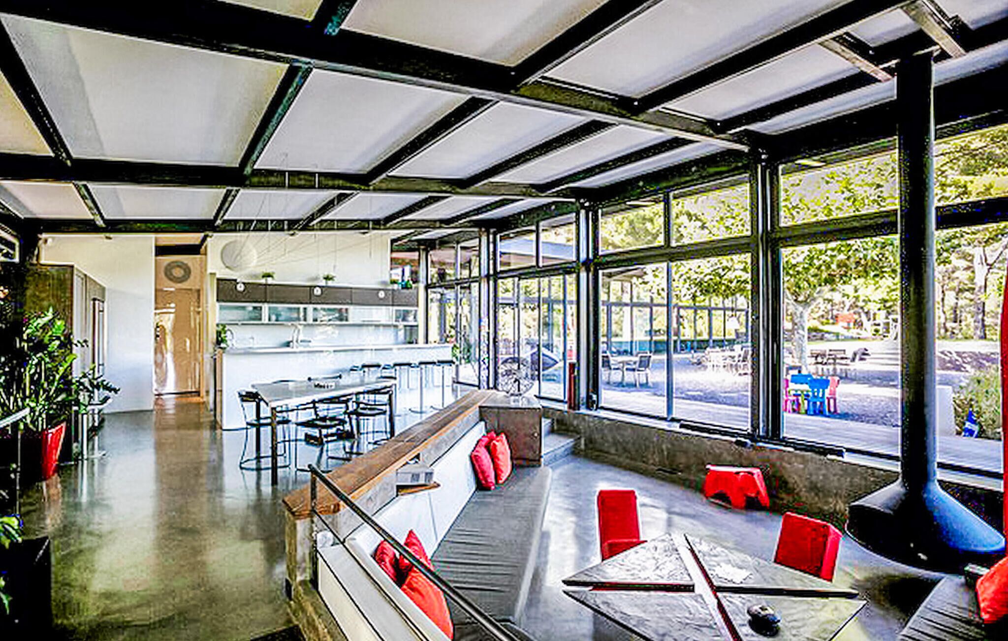 Um restaurante moderno com teto alto, grandes janelas e uma variedade de assentos, incluindo mesas e bancos.