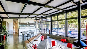 Un restaurante moderno con techo alto, ventanas amplias y una combinación de asientos, incluyendo mesas y bancos.