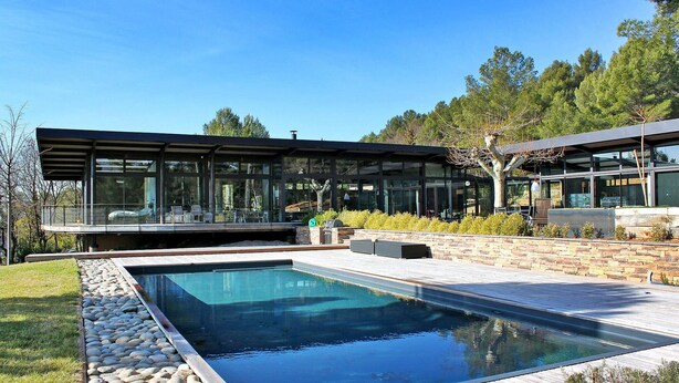 Una casa moderna con piscina, amplios ventanales de vidrio y un patio de piedra.