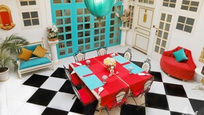 A room with a checkered floor, a dining table with red and blue tablecloths, a red sofa, and a turquoise hanging light fixture. - The Royal Hermitage (Jaipur)