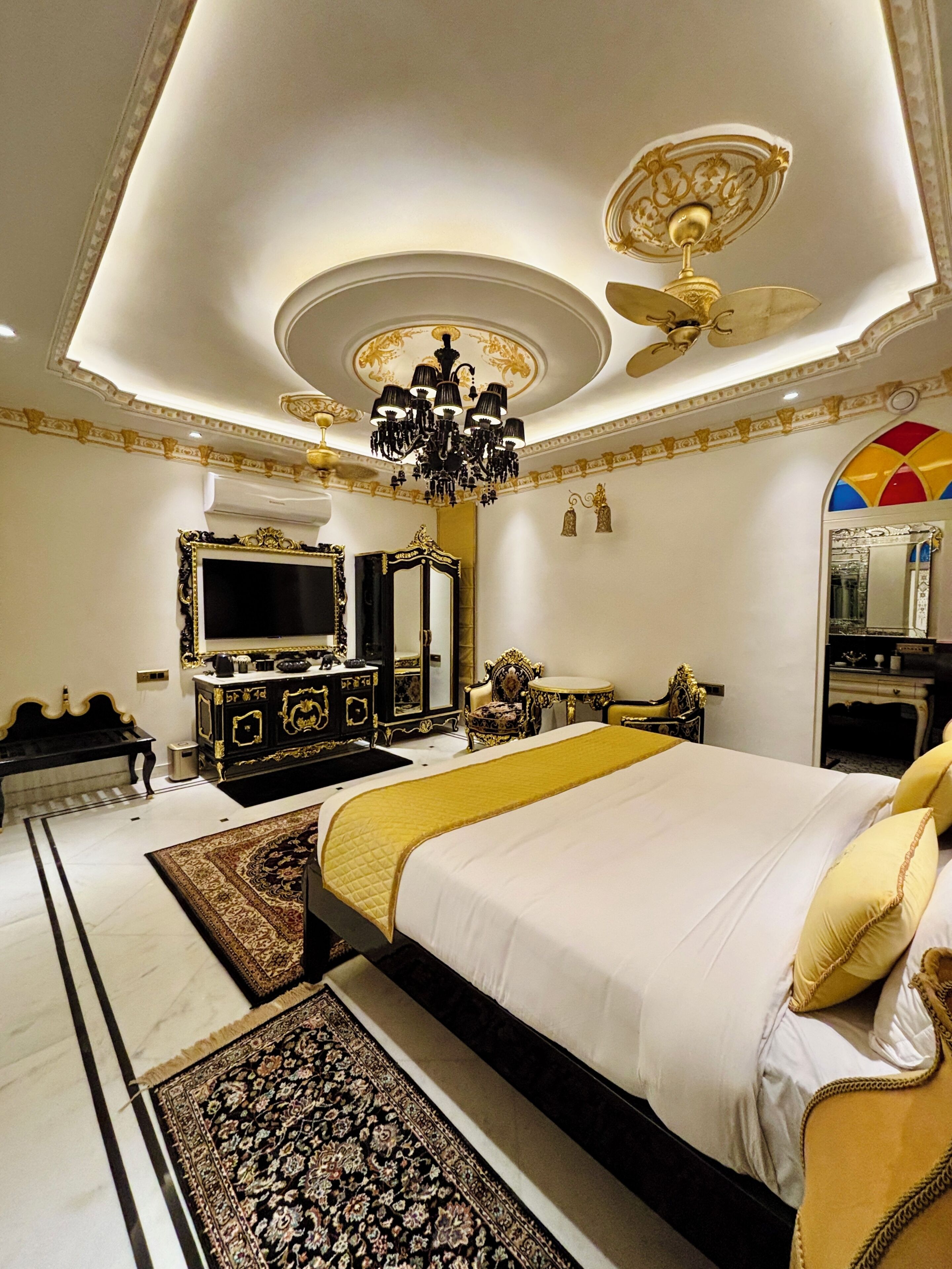 Une chambre à coucher luxueuse, dotée d’un grand lit, d’un lustre, d’un ventilateur de plafond et de meubles richement décorés.