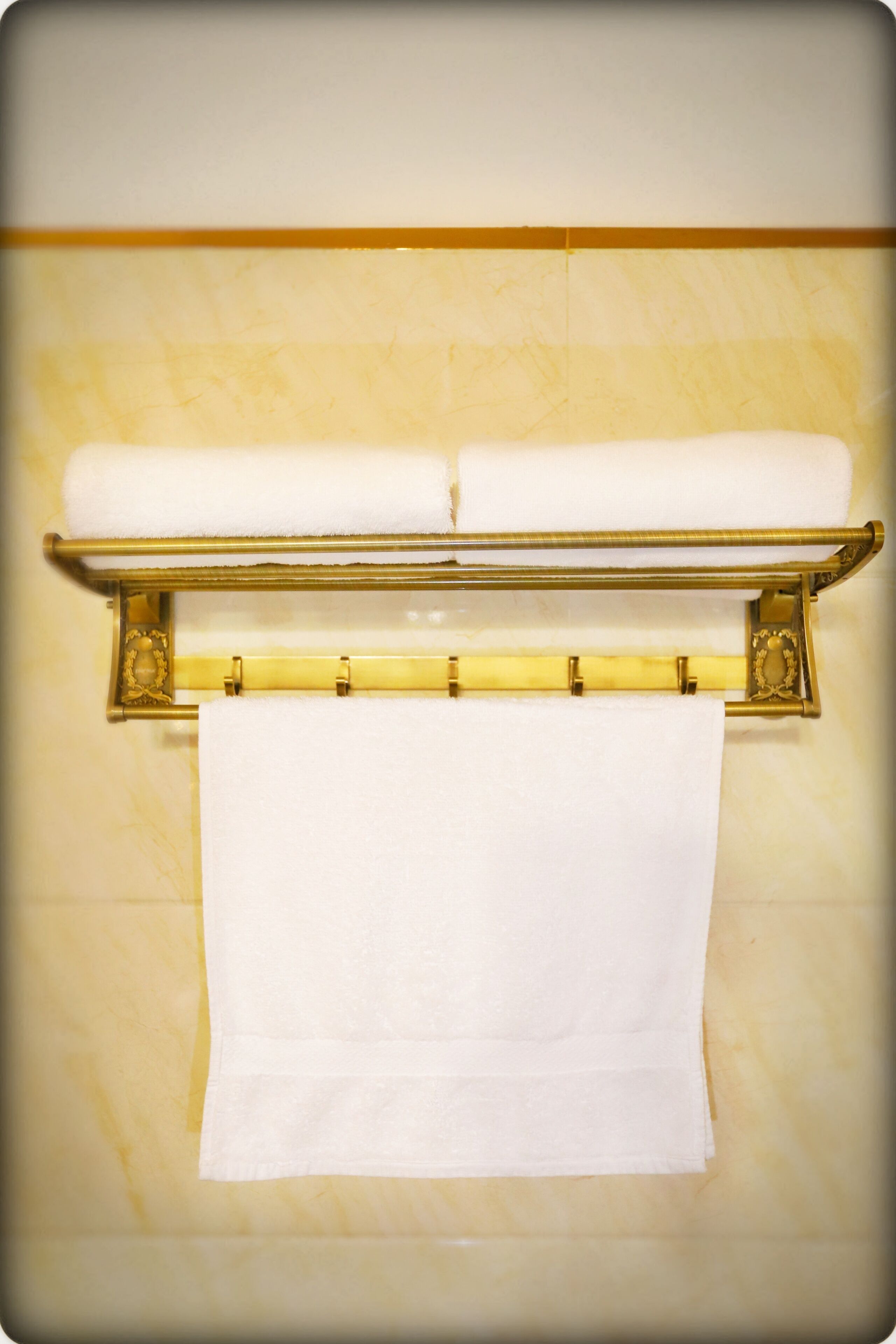 A bathroom with a gold towel rack holding two folded towels and a single towel hanging below.