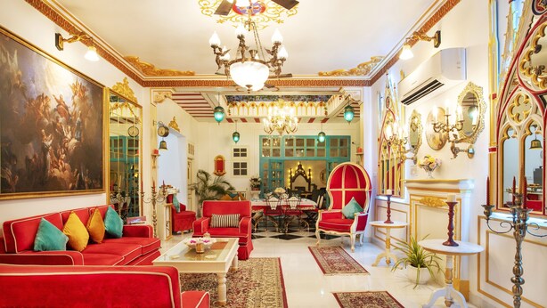 A luxurious room with a red sofa, ornate chandeliers, and a large mirror. - The Royal Hermitage (Jaipur)