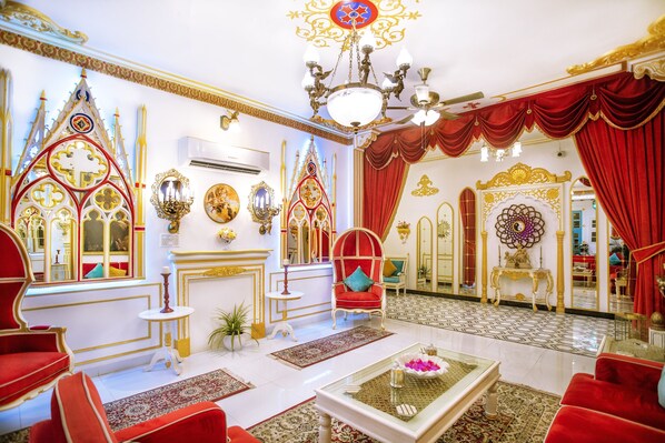 Una habitación lujosa con decoración elaborada, un candelabro, muebles rojos y un espejo grande.