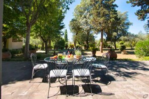 A patio with a round table and chairs, surrounded by trees and potted plants. - Villa Fortini by MMega (Bagno a Ripoli)