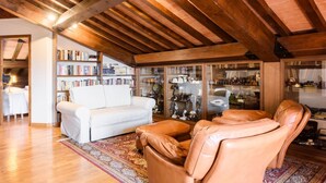 Un salon chaleureux avec un canapé blanc, un fauteuil en cuir et une bibliothèque remplie de livres et d’objets décoratifs.