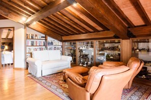A cozy living room with a white sofa, leather armchair, and a bookshelf filled with books and decorative items. - Villa Fortini by MMega (Bagno a Ripoli)