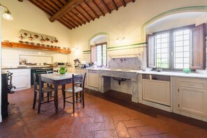 A spacious kitchen with a dining area, wooden ceiling beams, and a large window.