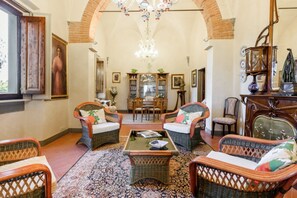 A spacious living room with wicker furniture, a chandelier, and a view of the dining area.