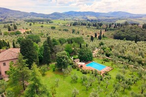 A villa with a swimming pool surrounded by lush greenery and hills in the background.