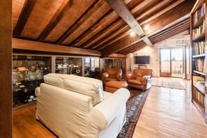 A spacious living room with a high ceiling, leather sofas, a television, and a bookshelf.