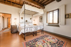 A four-poster bed with a lace canopy, a patterned rug, and a window with a view.